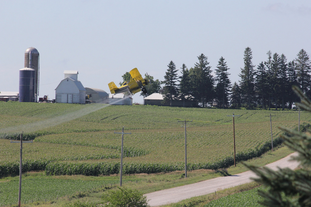 a plane sprays pesticides over a farm