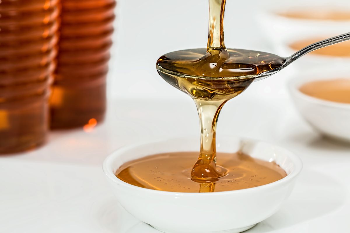 Honey being poured over a spoon into a white ceramic bowl.