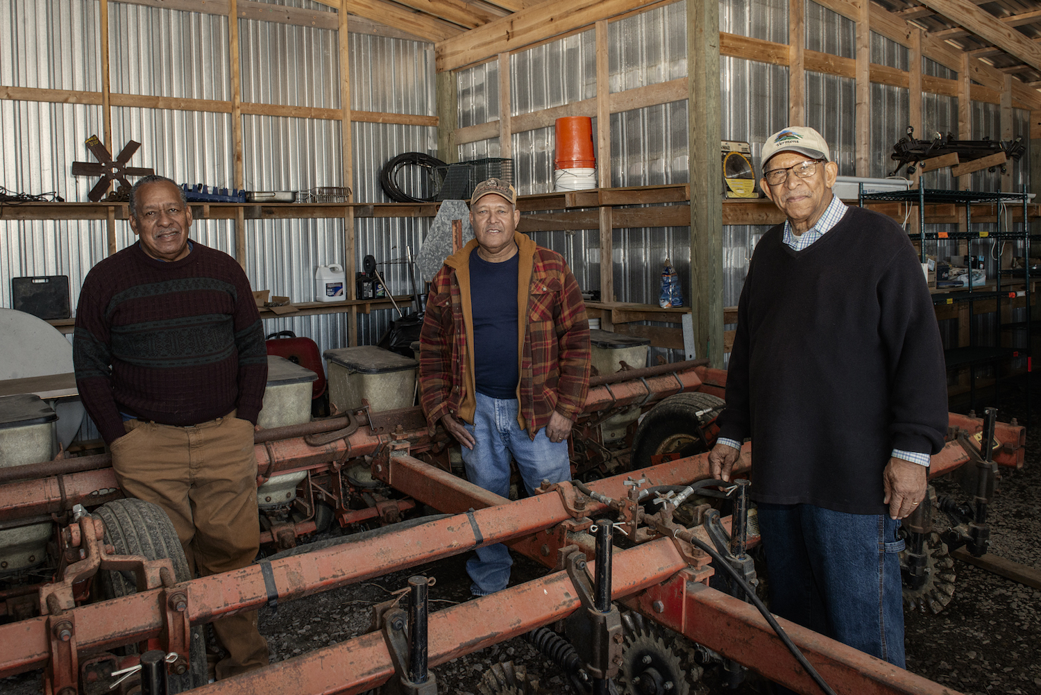 From left to right: The Wright brothers, John, Herbert and Lloyd, stand by a large planter housed in the barn with other farming equipment.