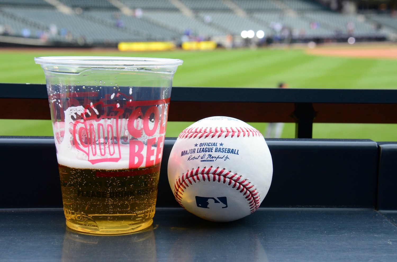 A plastic cup of beer and a baseball at a park