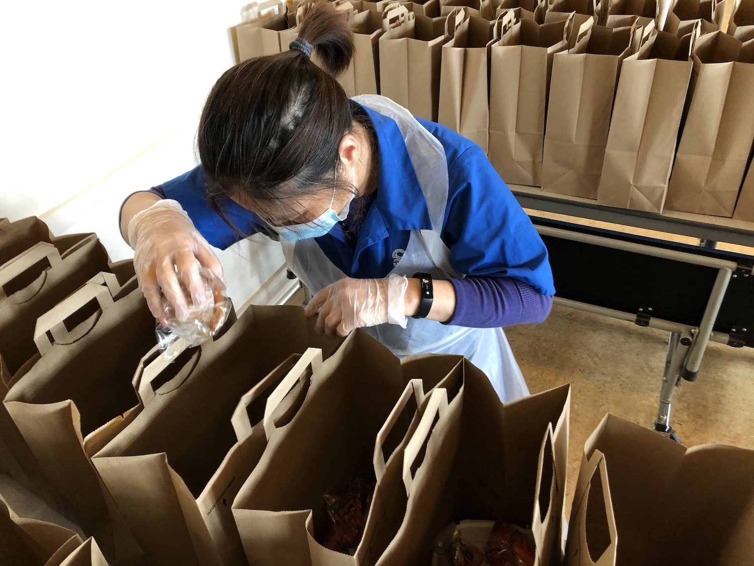 A SFUSD worker in PPE packs meal kits during the Covid-19 pandemic.