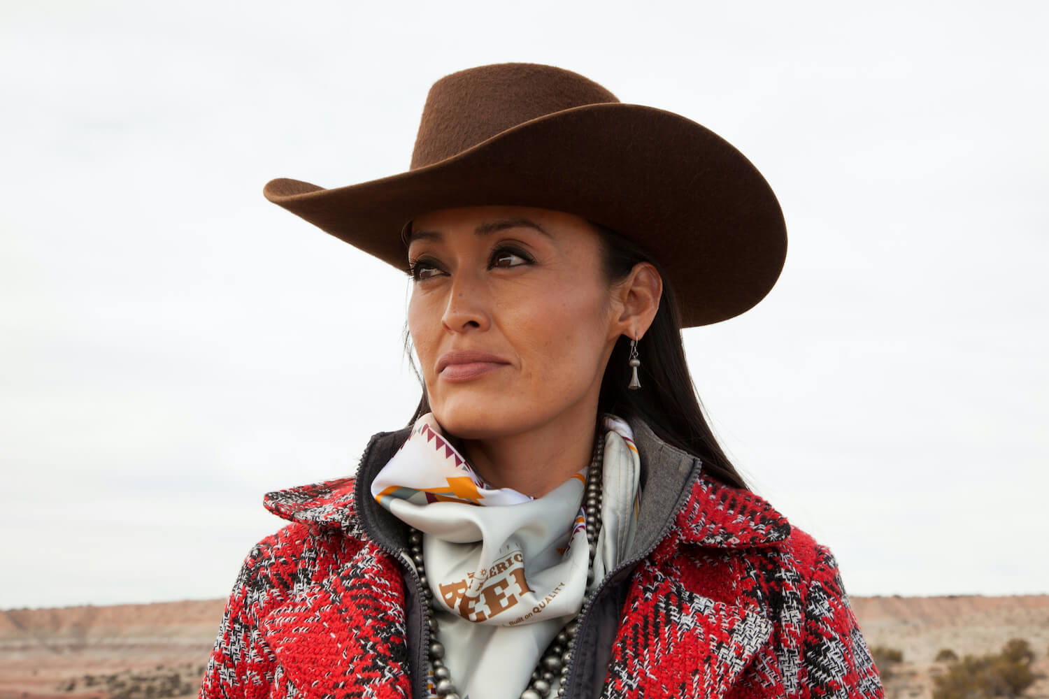 A woman wearing a cowboy hat and red flannel looks away from the camera. June 2020