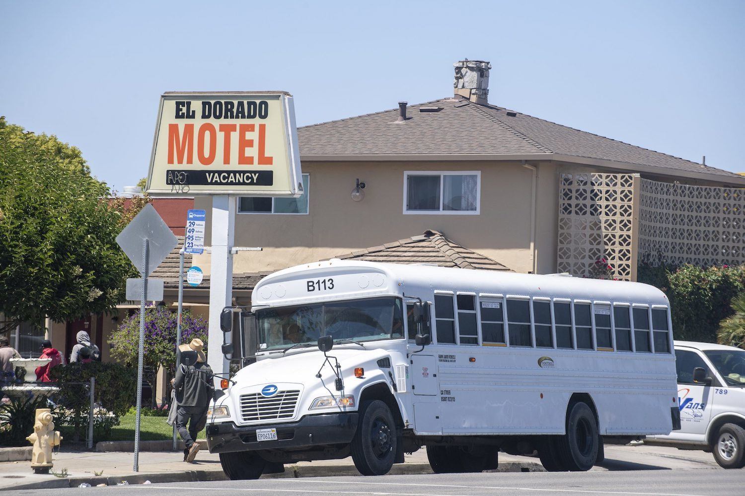 A white bus stops in front of El Dorado Motel with workers exiting. August 2020