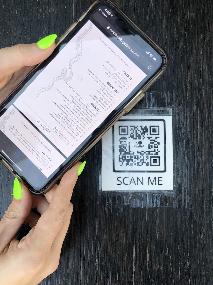 hands hold a phone with a digital menu and QR code. September 2020