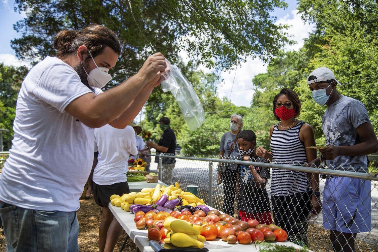 Jason Rolland sells vegetables to Gretchen Barron and her family at the Pinehurst Farmers Market on Wednesday, July 22, 2020, in Columbia, S.C.