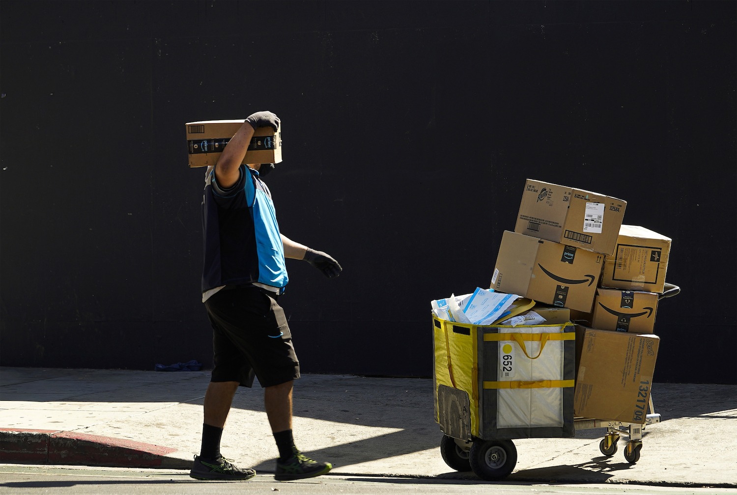 In this Oct. 1, 2020, photo an Amazon worker wears a mask and gloves as he delivers boxes downtown Los Angeles Friday, Oct. 2, 2020. Amazon says that nearly 20,000 of its workers have tested positive or been presumed positive for the virus that causes COVID-19. Amazon says in a corporate blog Thursday that it examined data from March 1 to Sept. 19 for its 1.37 million workers at Amazon and Whole Foods Market. It said that it compared COVID-19 case rates to the general population, as reported by Johns Hopkins University for the same period. Based on that analysis, if the rate among Amazon and Whole Foods employees were the same as it is for the general population rate, it estimated it would have seen 33,952 cases among its workforce.