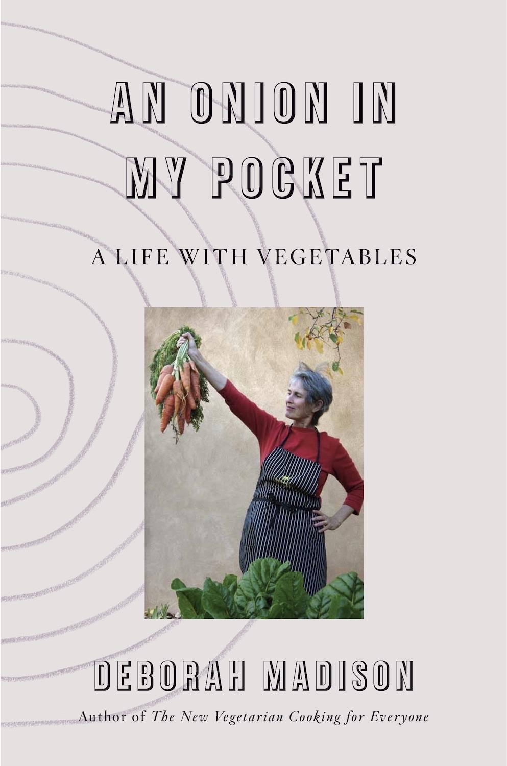 An Onion In My Pocket, A Life With Vegetables cover by Deborah Madison, holding a bunch of carrots and wearing a black and white striped apron. November 2020