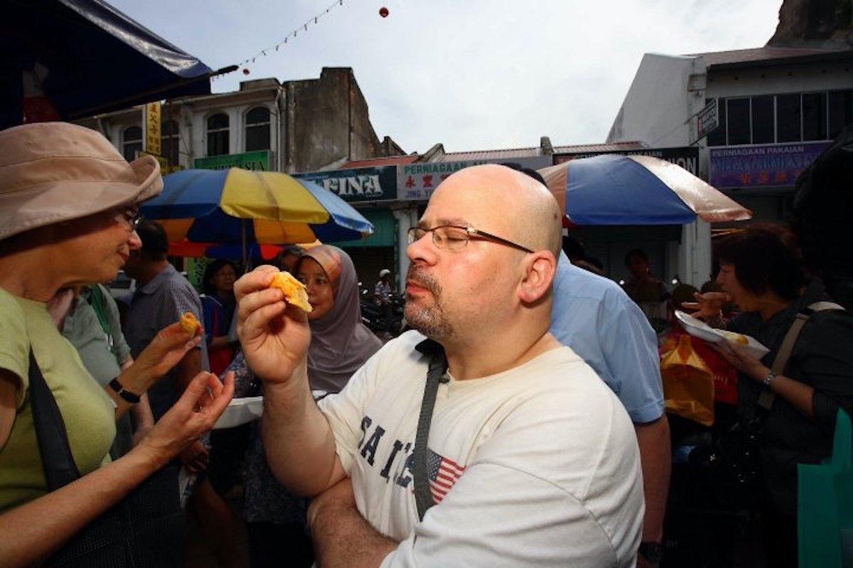 Bret Thorn stands on a crowded street holding a piece of durian. January 2021