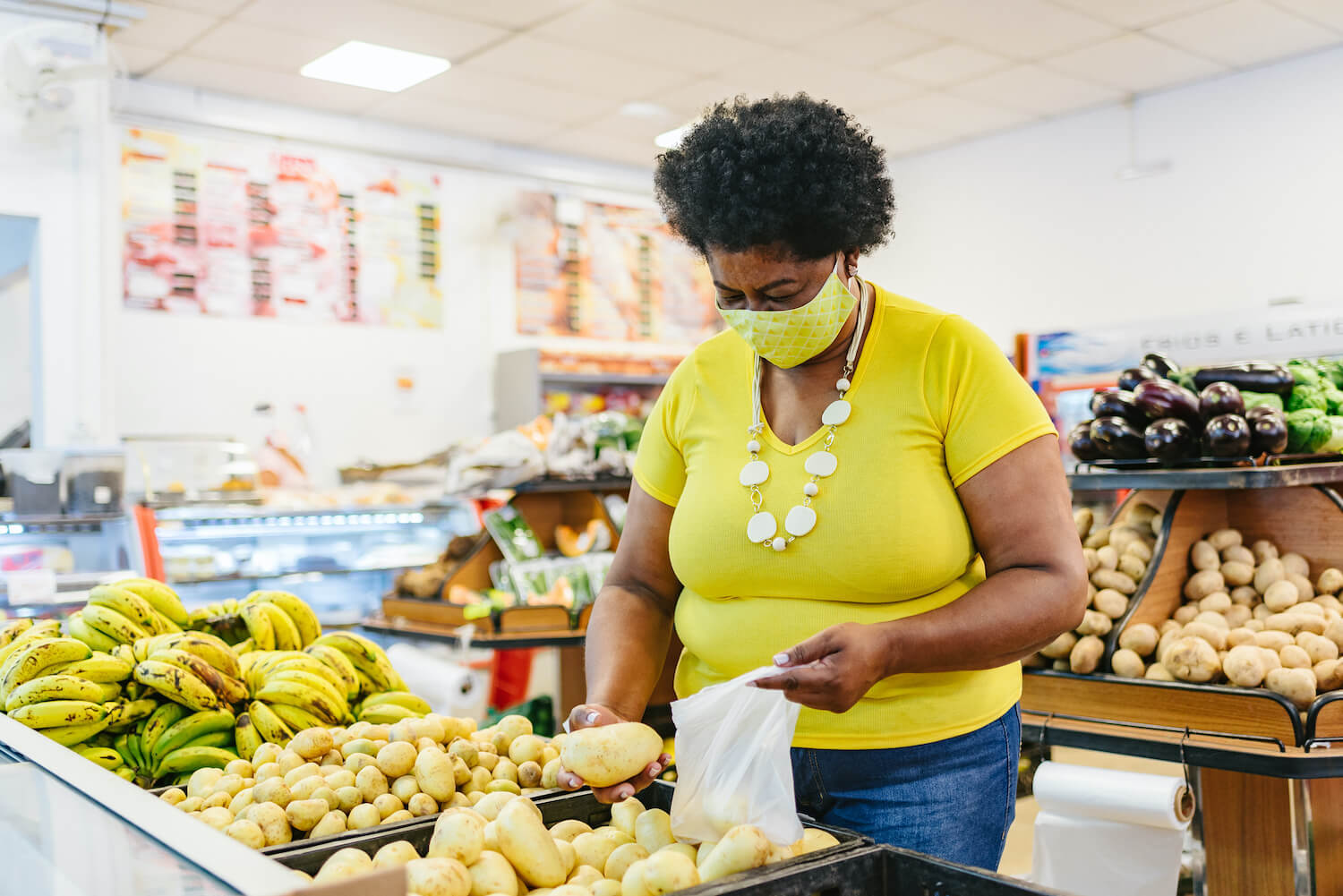 A Black woman wearing a mask shops for produce in a grocery store. January 2021