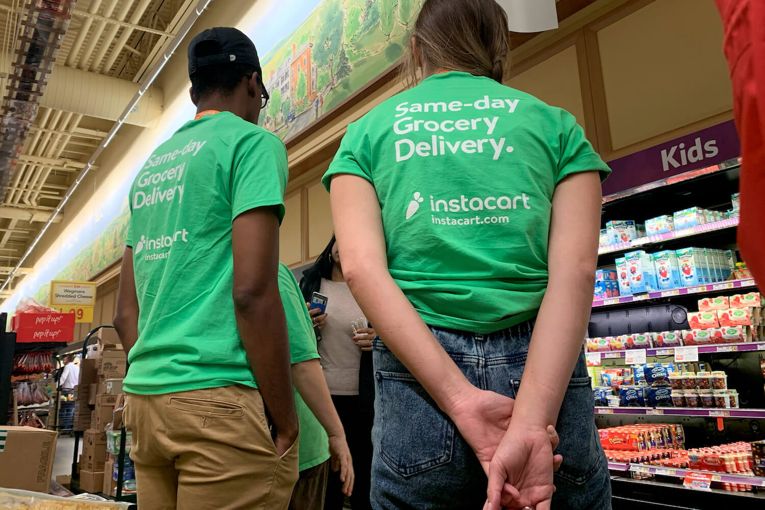 Two gig economy Instacart workers face their backs to the camera inside a grocery store. January 2021