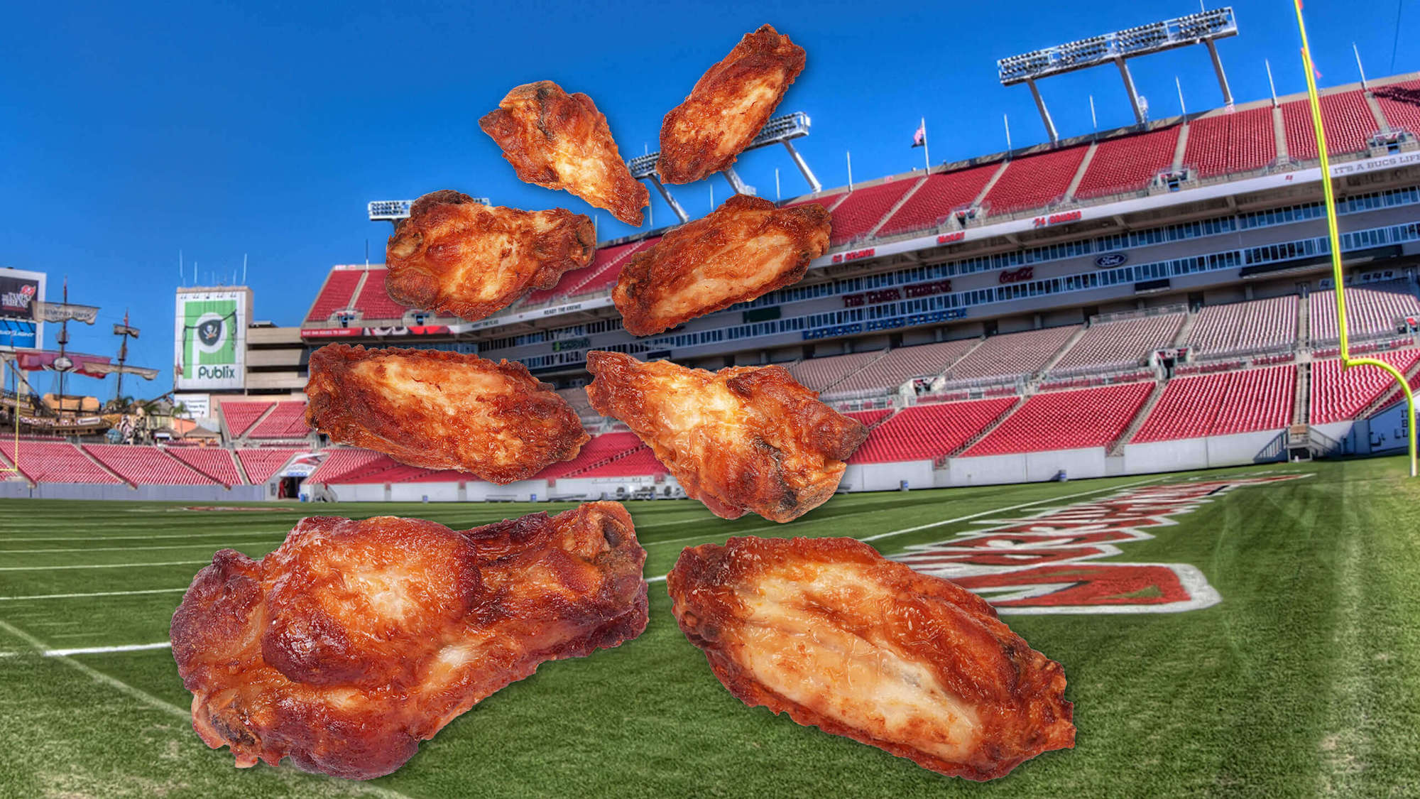 Cut outs of chicken wings fall from the sky in front of the Super Bowl stadium background. February 2021