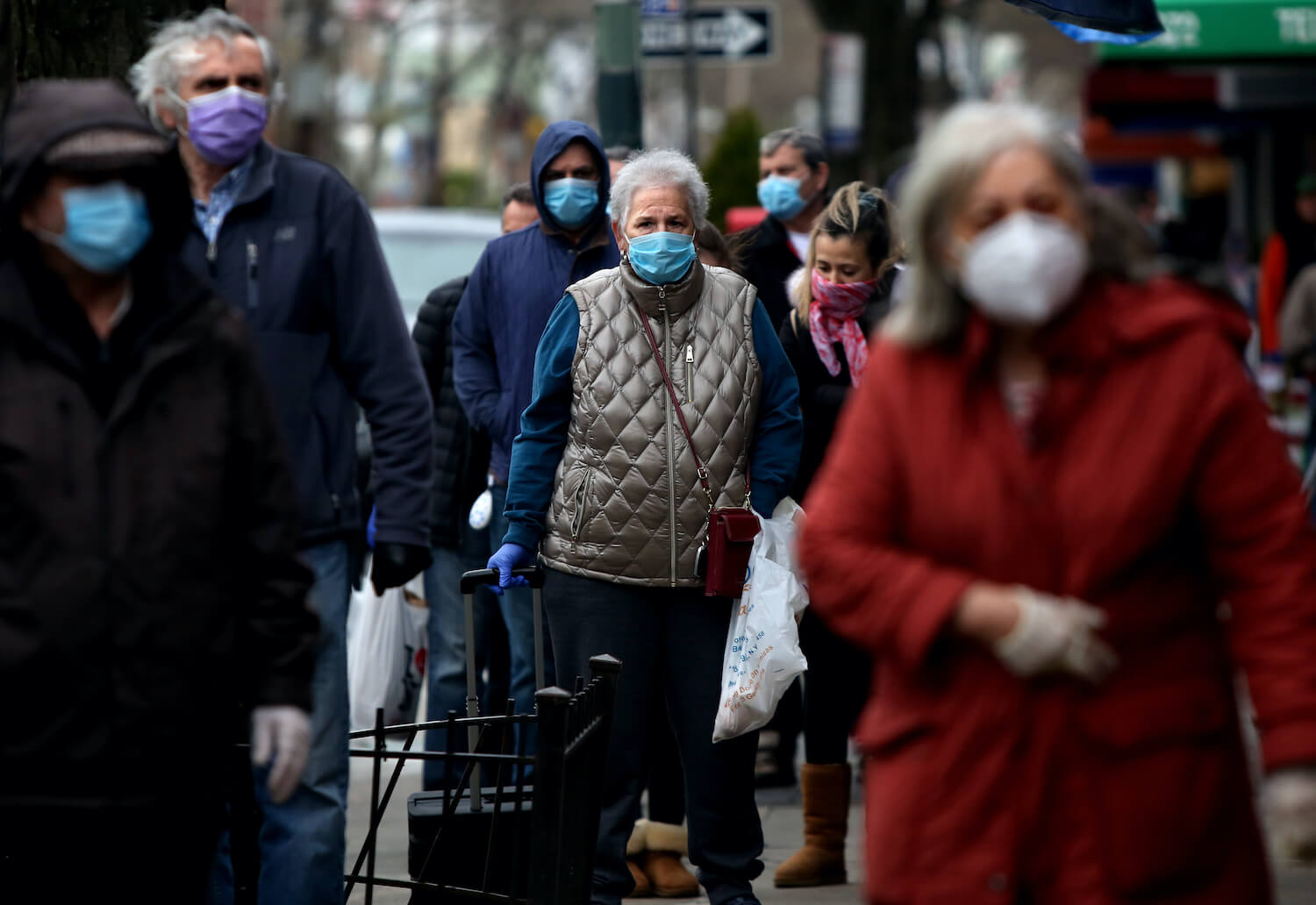 A line of masked people wait to pick up food from Biancardis on Arthur Ave. in the Bronx, NY, on April 10, 2020. March 2021