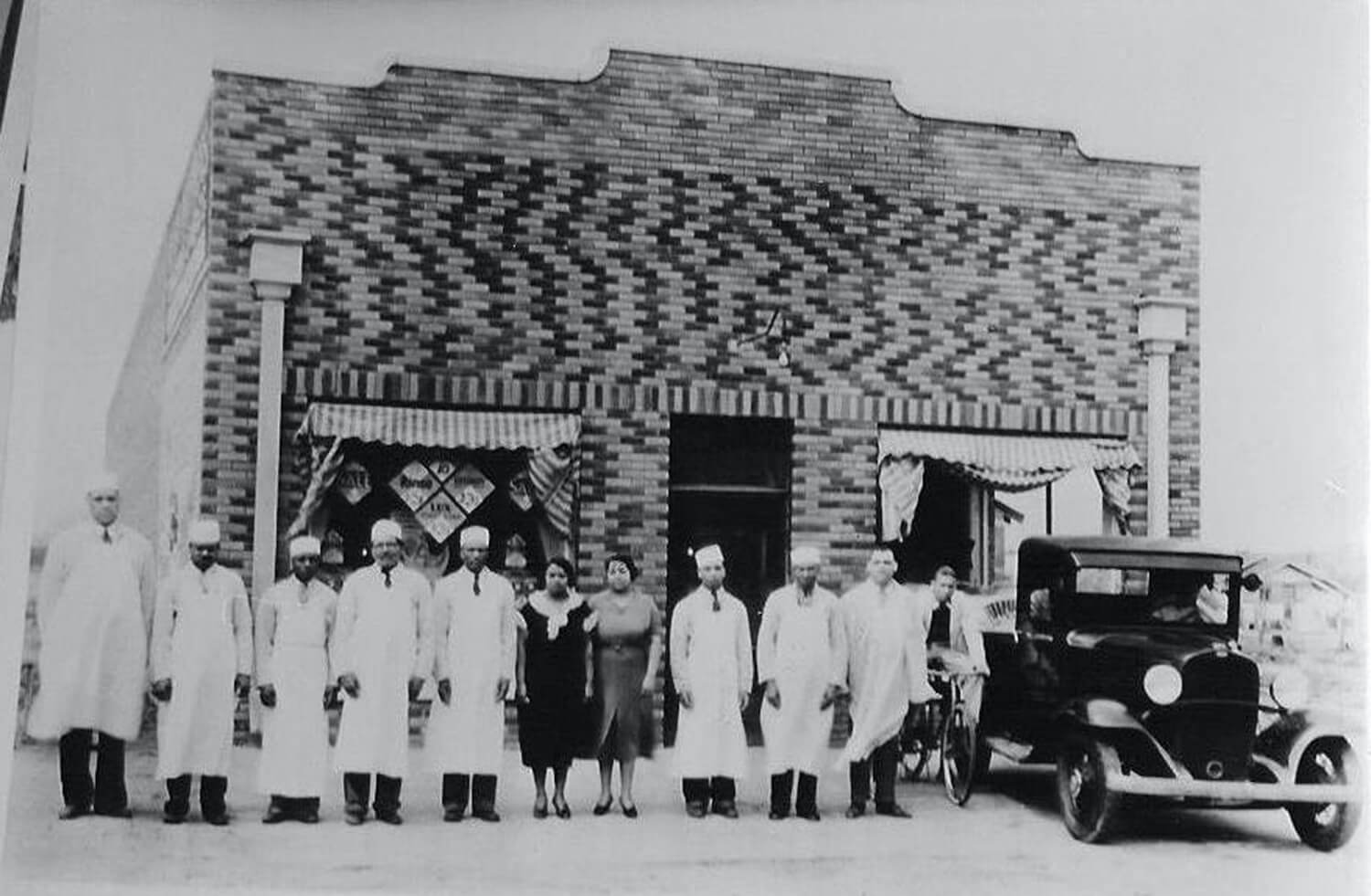 Portrait of staff members as they stand in front of Mann Brothers Grocery and Market (at the intersection of Lansing Avenue and Oklahoma Street), Tulsa, Oklahoma, 1940s. May 2021