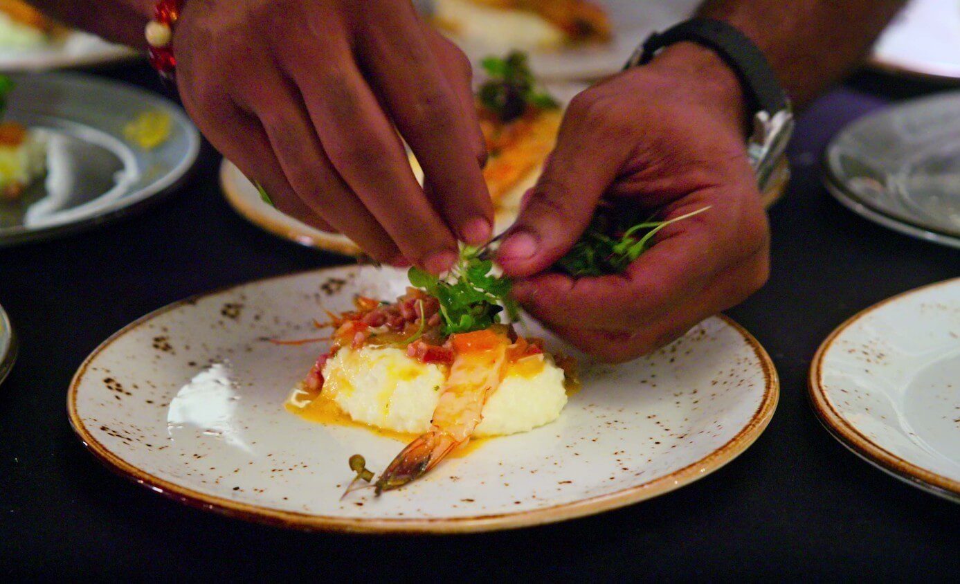 Hands plating shrimp and grits with micro greens. A still from the Netflix series, 