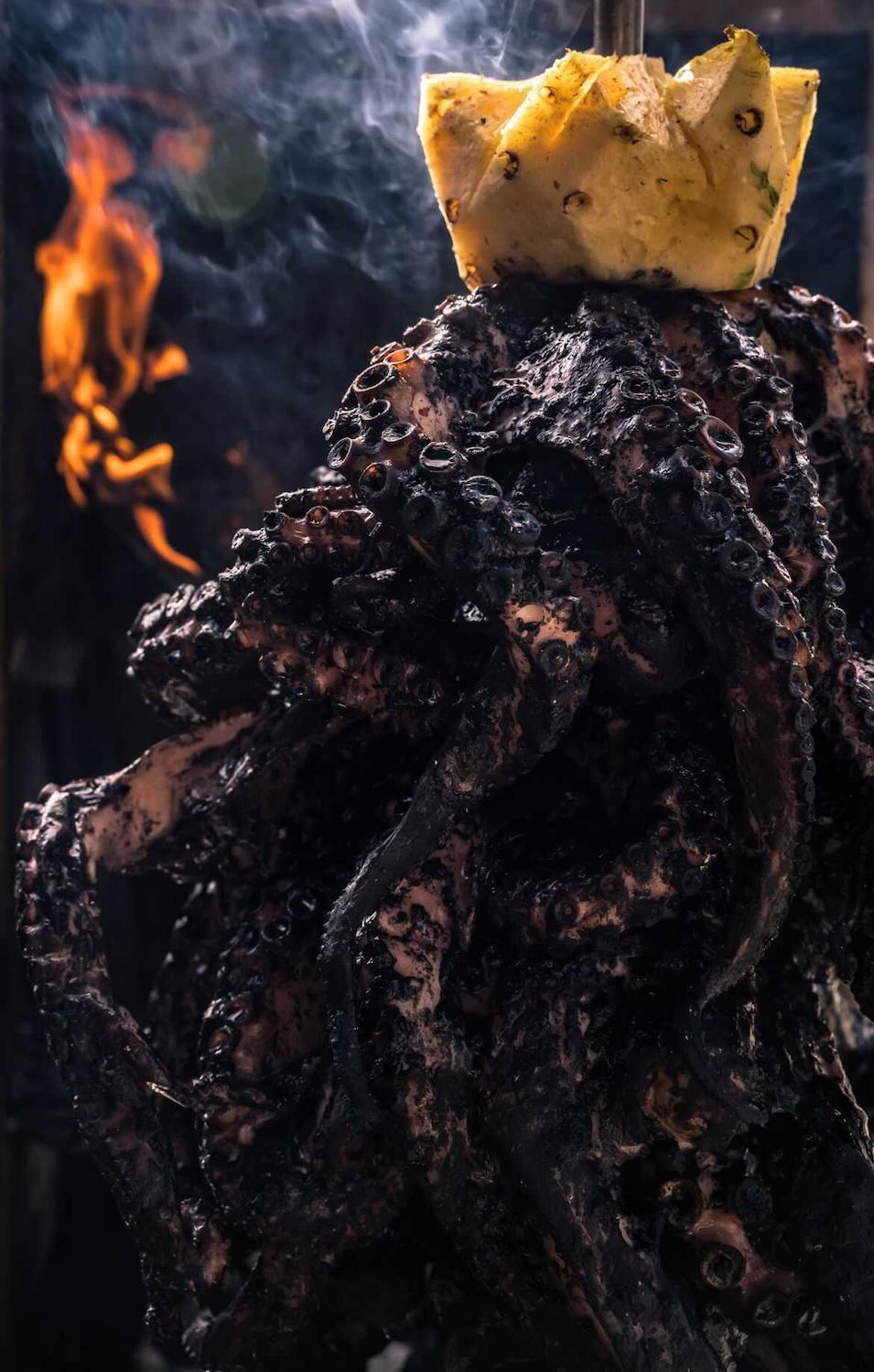 Octopus al-pastor charred with pineapple on top and fire and smoke on the left from Evil Cooks. July 2021