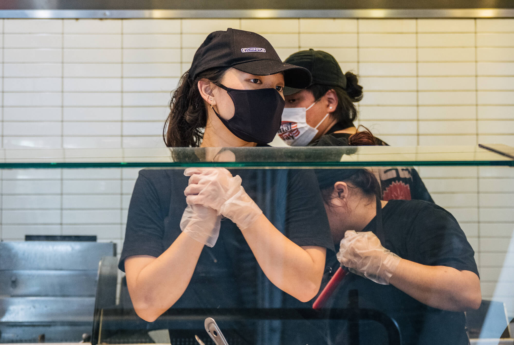Masked Chipotle employees stand behind the counter. July 2021