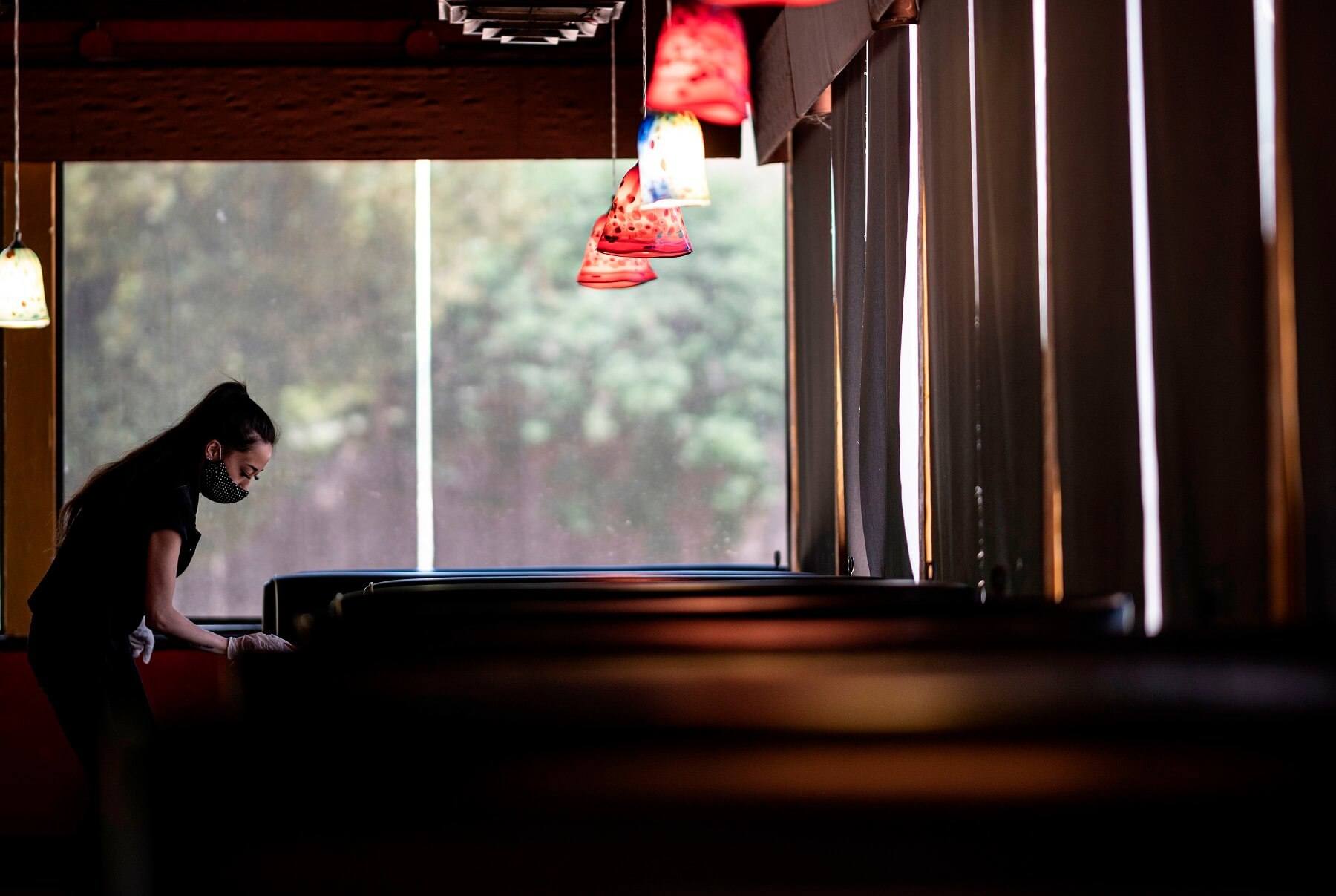 waitress wearing a mask and gloves disinfects a table in a Restaurant on May 5, 2020 in Stillwater, Oklahoma. July 2021