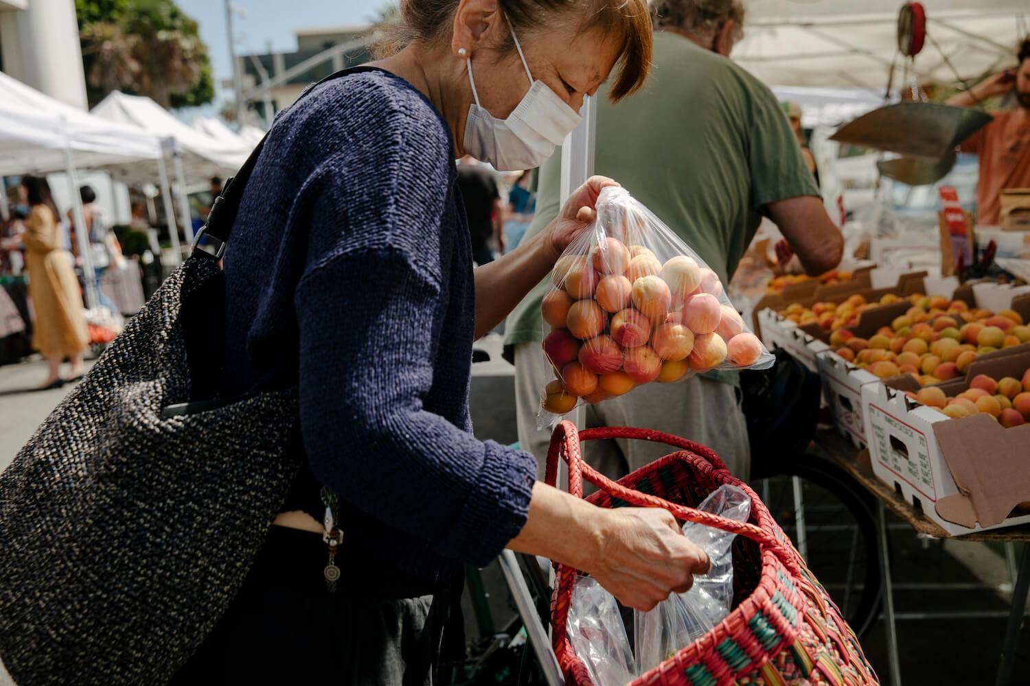 Woman packing bag of apricots into basket at Santa Monica market. August 2021
