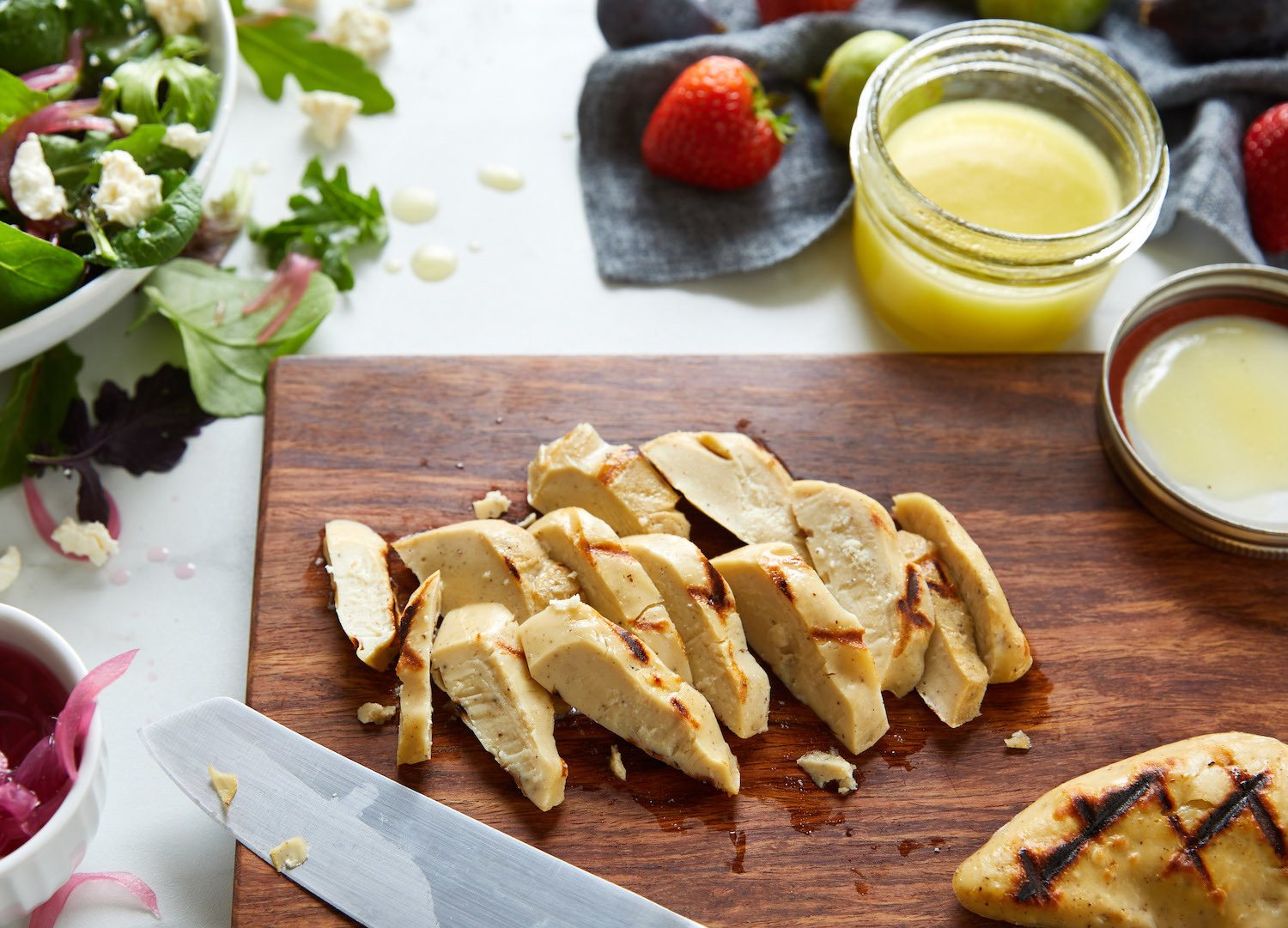 Cultured chicken on cutting board with salad in the background. September 2021