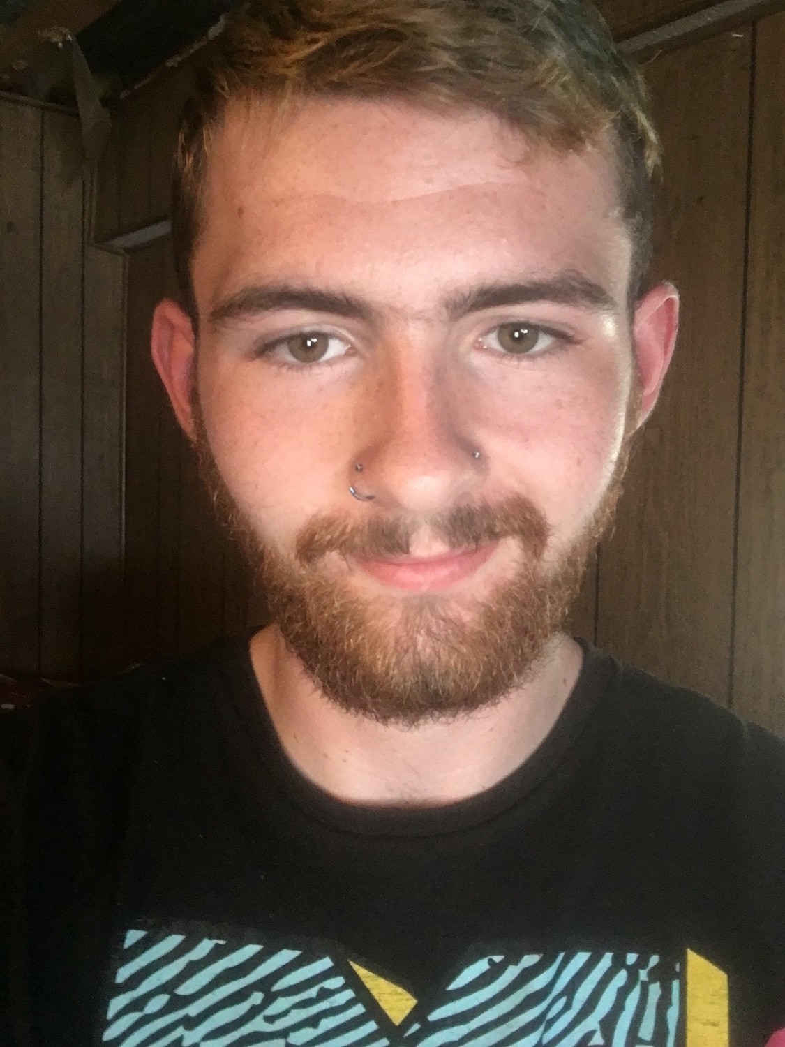 Selfie of Mathew Honeycutt wearing a black t-shirt, facial hair and nose piercings. September 2021