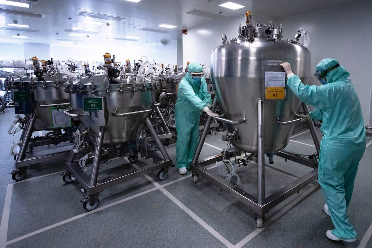 Lab technicians dedicated to the vaccines formulation, wearing Personal Protective Equipment (PPE), move stainless steel tanks for manufacturing vaccines preparations before the syringe filling phase, at a French pharmaceutical company Sanofi's world distribution centre in Val-de-Reuil on July 10, 2020. (Photo by JOEL SAGET / AFP) (Photo by JOEL SAGET/AFP via Getty Images)