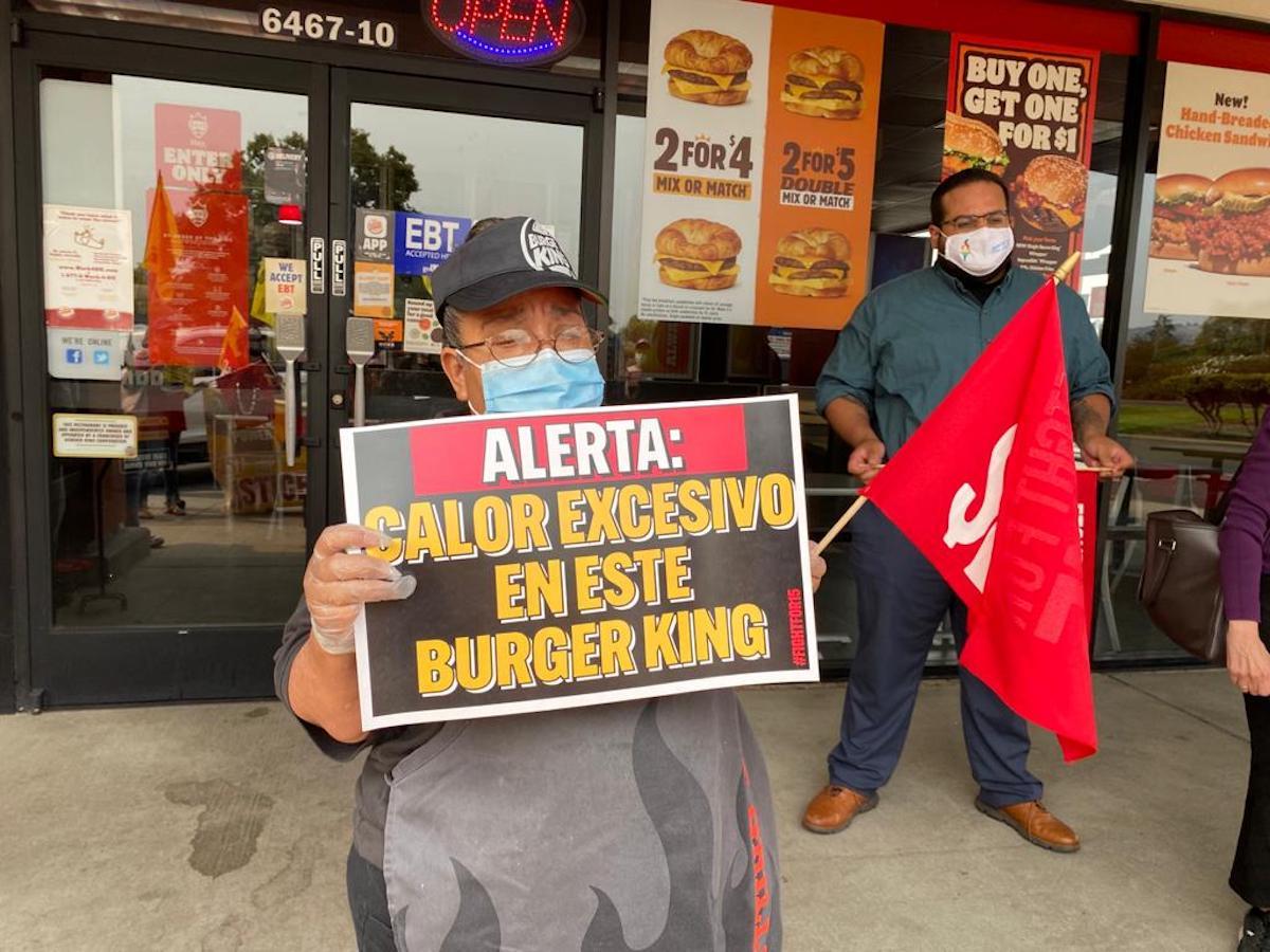 A worker striking in front of Burger King holding a sign in Spanish that translates to 