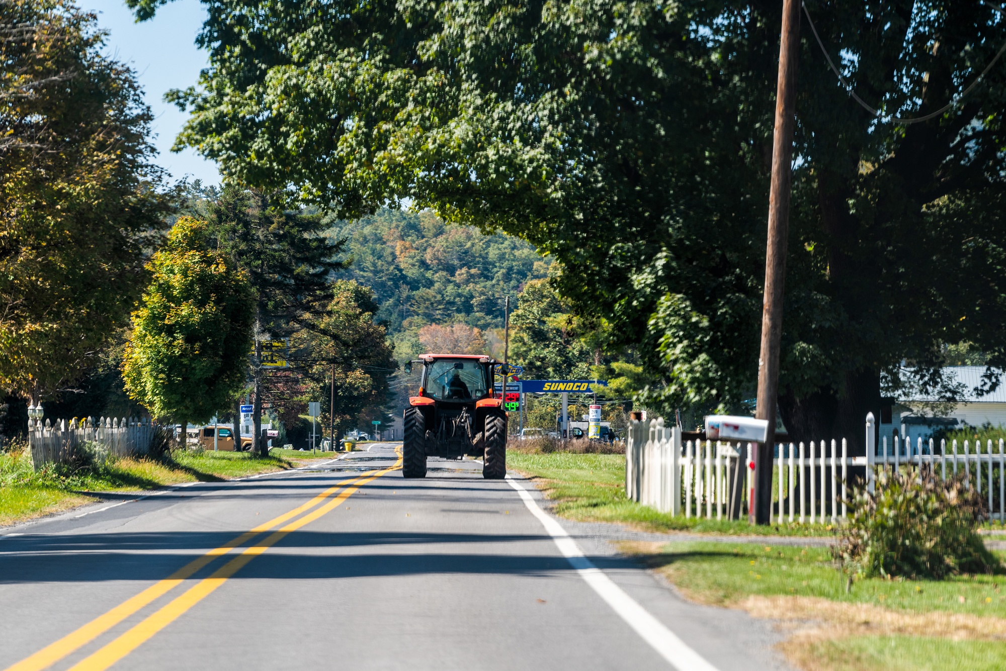Farmer tractor driving on paved rural countryside highway road in Green Bank city small science town village in West Virginia. October 2021