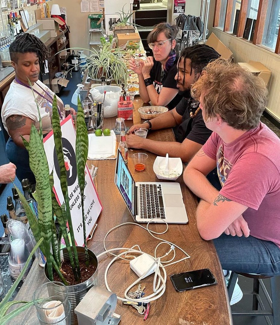 Meeting of the bar team at Red Emma. Worker-owners sit around a table with laptops and plants.October 2021