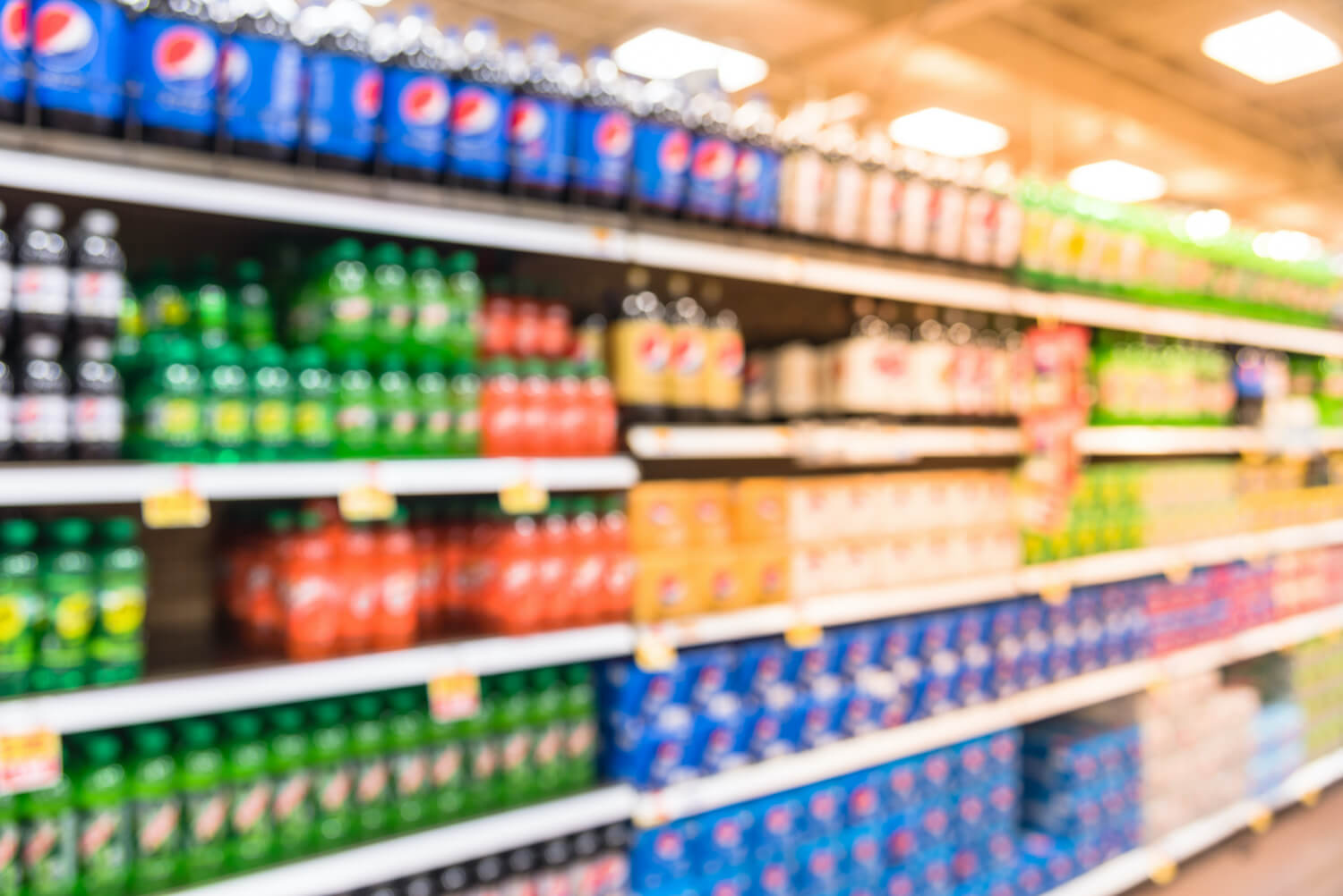 A blurred image showing a row of sugary drinks in a grocery store. October 2021