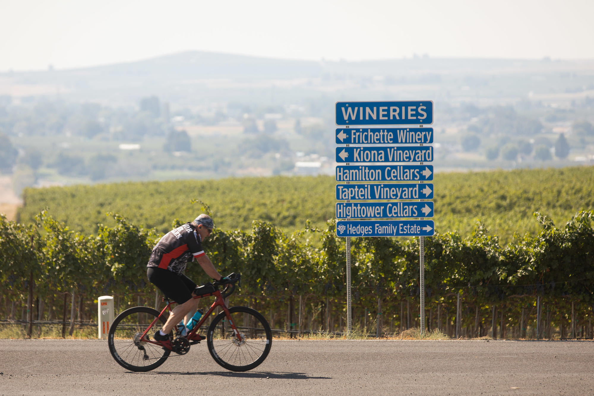 A cyclist rides by a sign directing drivers to the wineries in the Yakima Valley. October 2021