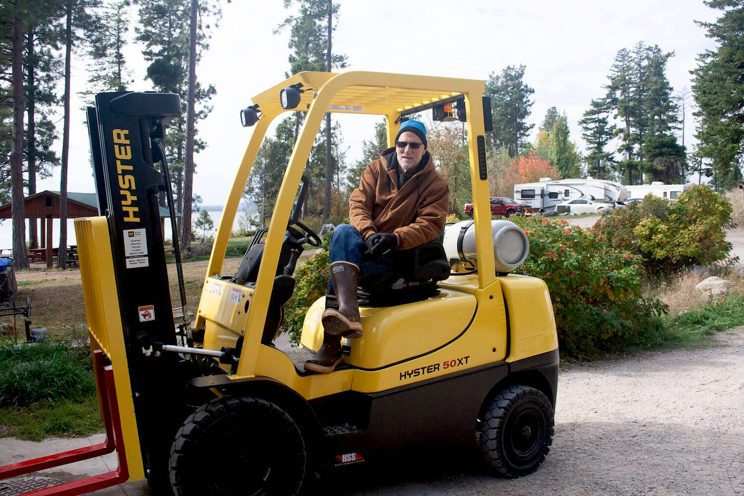 Barry Hansen the fisheries biologist for the CSKT sits on a yellow tractor wearing a brown coat, blue beanie, and boots. November 2021