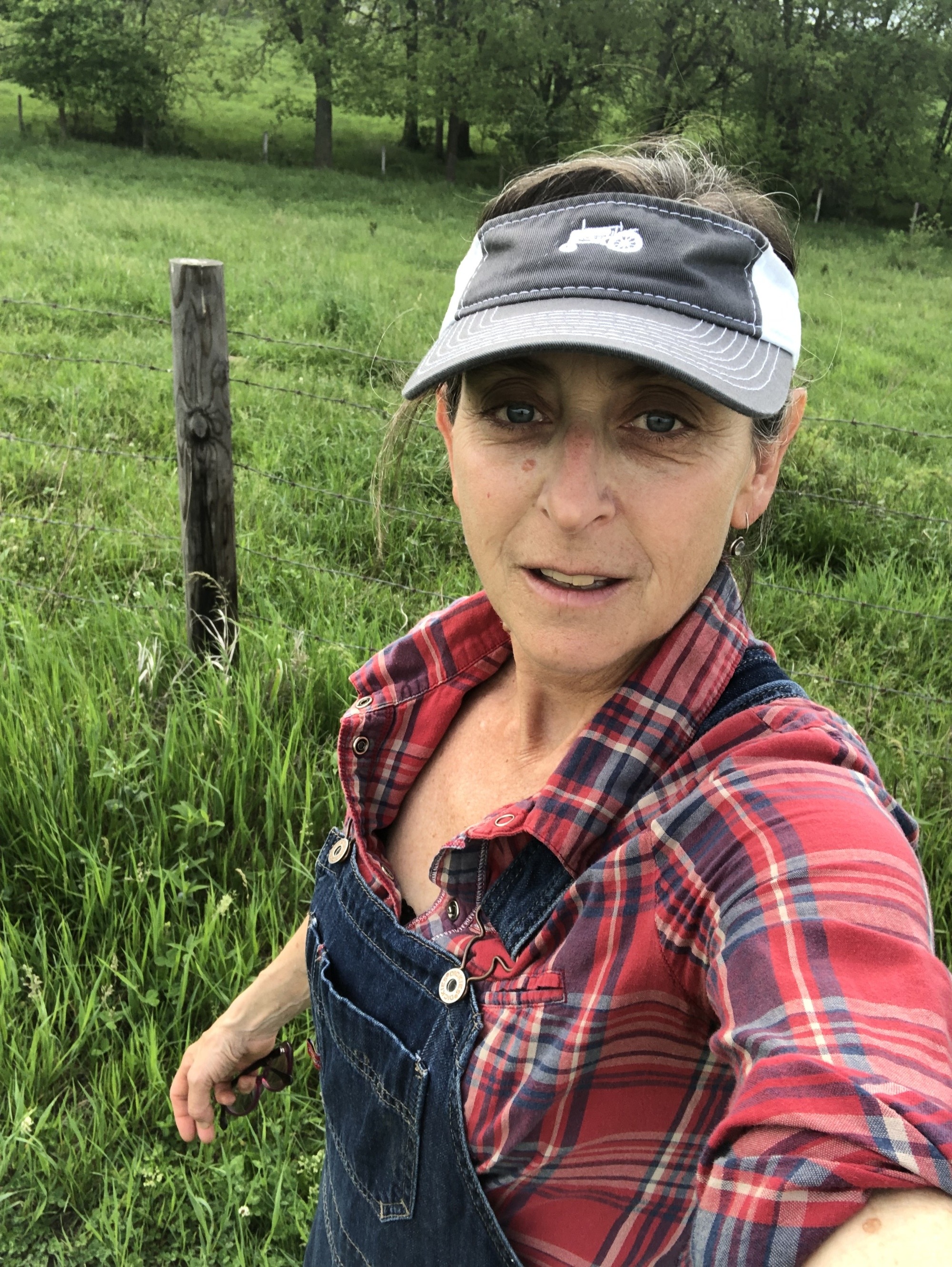 Beth Hoffman takes a selfie while in overalls next to a green field and a barbed wire fence. November 2021
