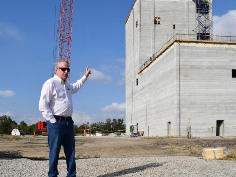 Man in white shirt and blue jeans stands in front of construction site with blue sky in background december 2021.