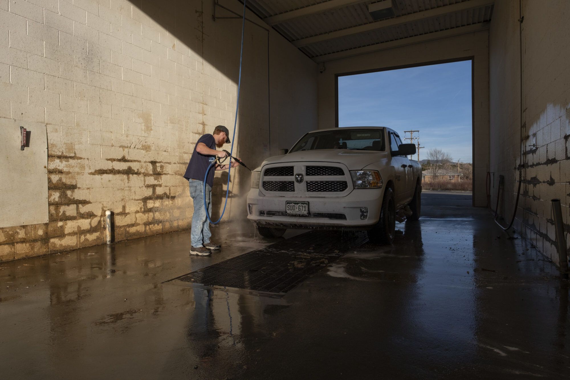 Man in jeans power washes a white dodge truck on sunny day December 2021.