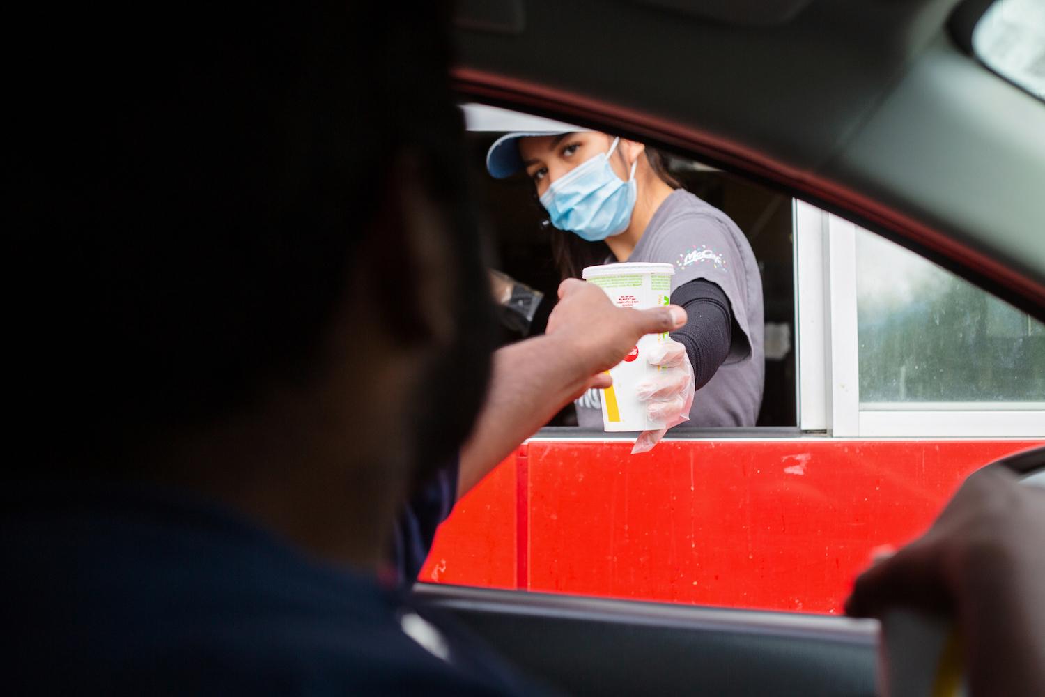 A man reaches for his food at the McDonalds drive-thru window as the employee wears a mask for protection - May 17, 2020.