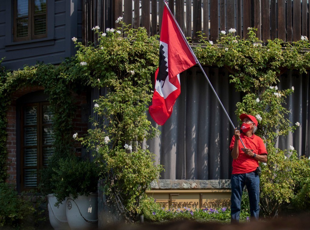 A demonstrator waves a red UFW flag while wearing a red shirt, hat, and mask behind a building January 2022.