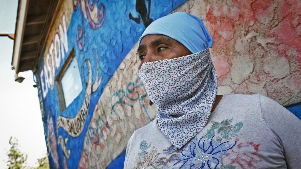 Margarita Amador wears a patterned bandana over face with blue crackled wall behind January 2022.