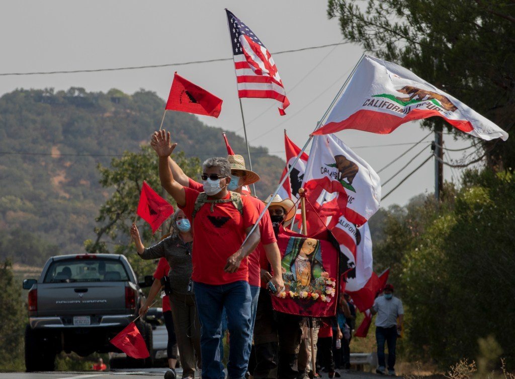 Protestors in red shirts and hats with flags wave to passerbys such as a gray truck in Yountville, CA January 2022.