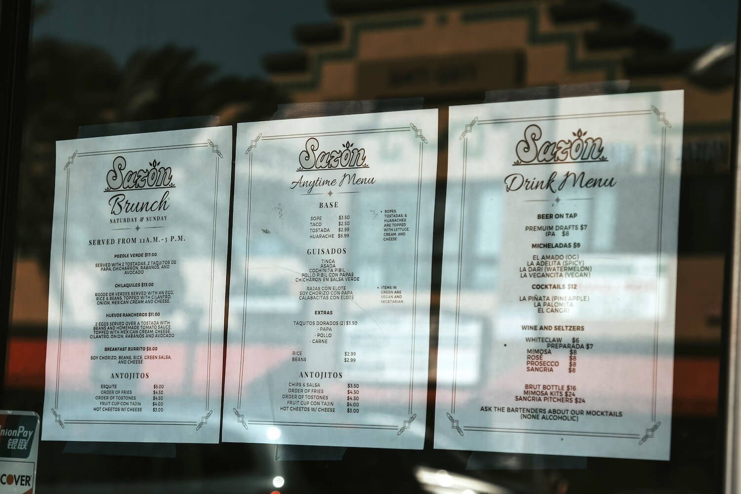 A photo of Sazón's menu with a reflection of the street. January 2022