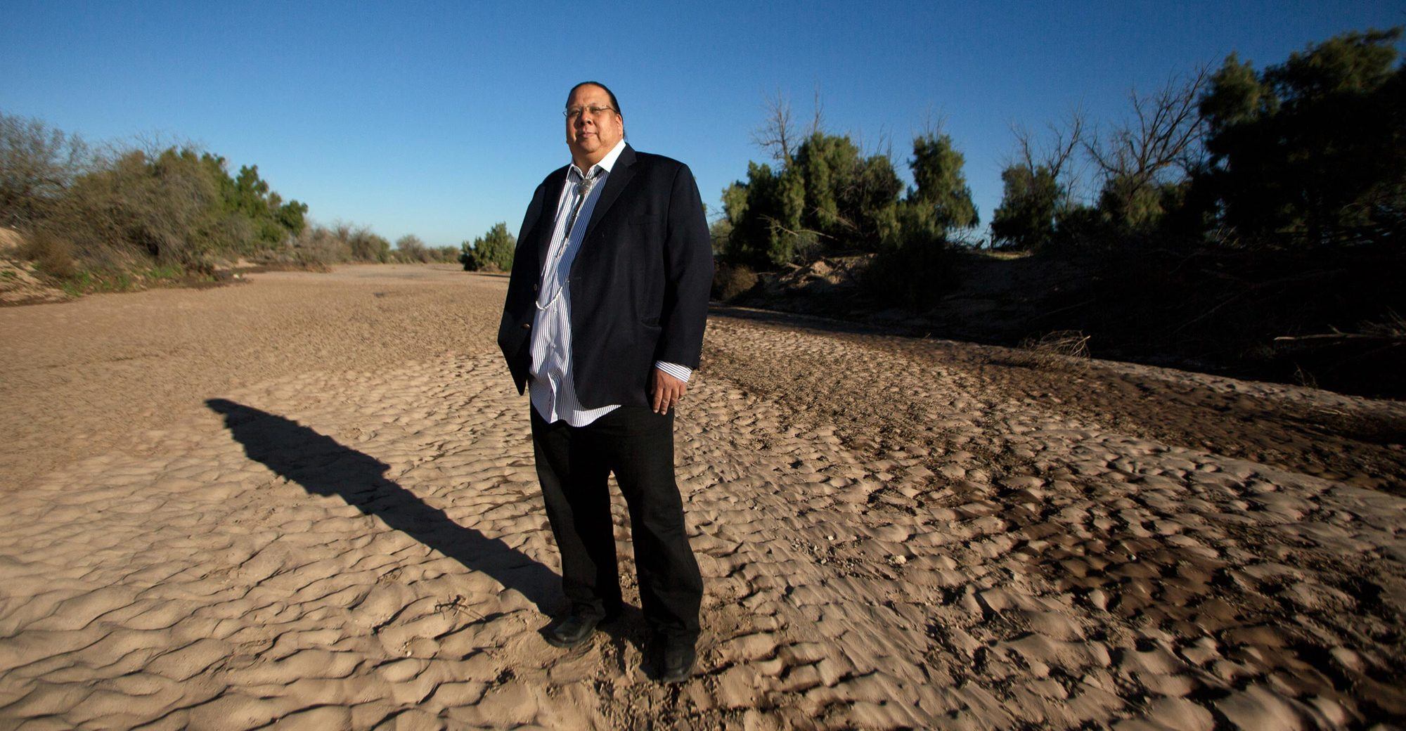 Gov. Stephen Roe Lewis, the leader of the Gila River Indian Community, stands in a suit in a patch of desert March 2022.