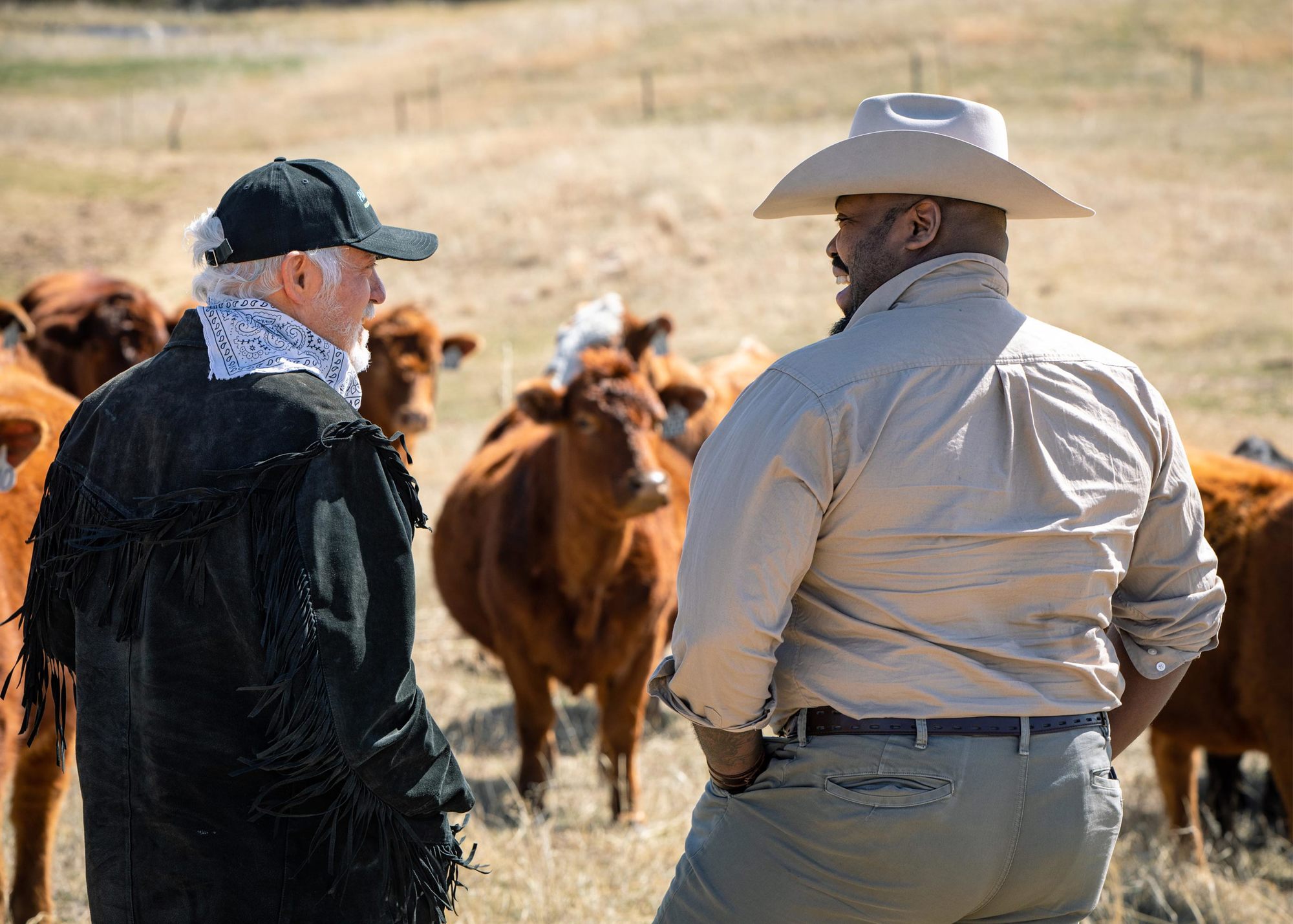 Johnson and Dave Hutchinson talk with hats on and cattle blurred in the background April 2022.
