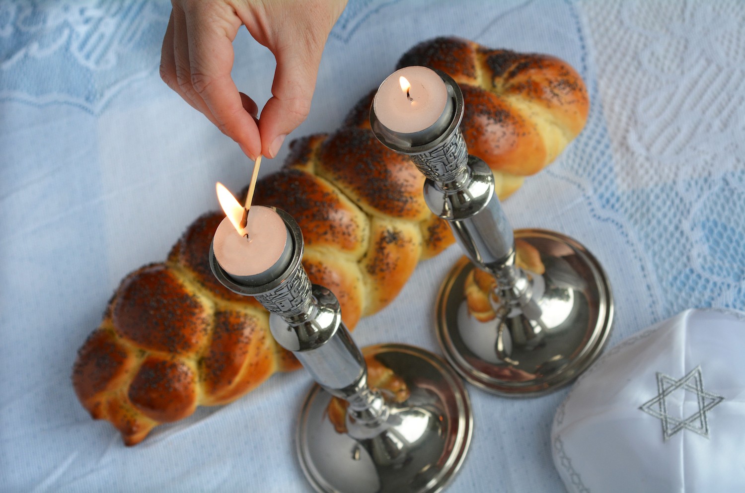 Shabbat eve table.Woman hand lit Shabbath candles with uncovered challah bread and kippah.